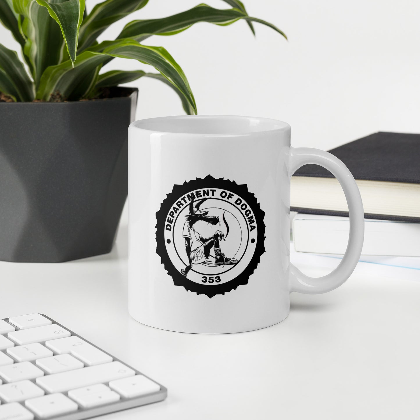 White mug with 'Department of Dogma' design on a desk with a plant and books in the background