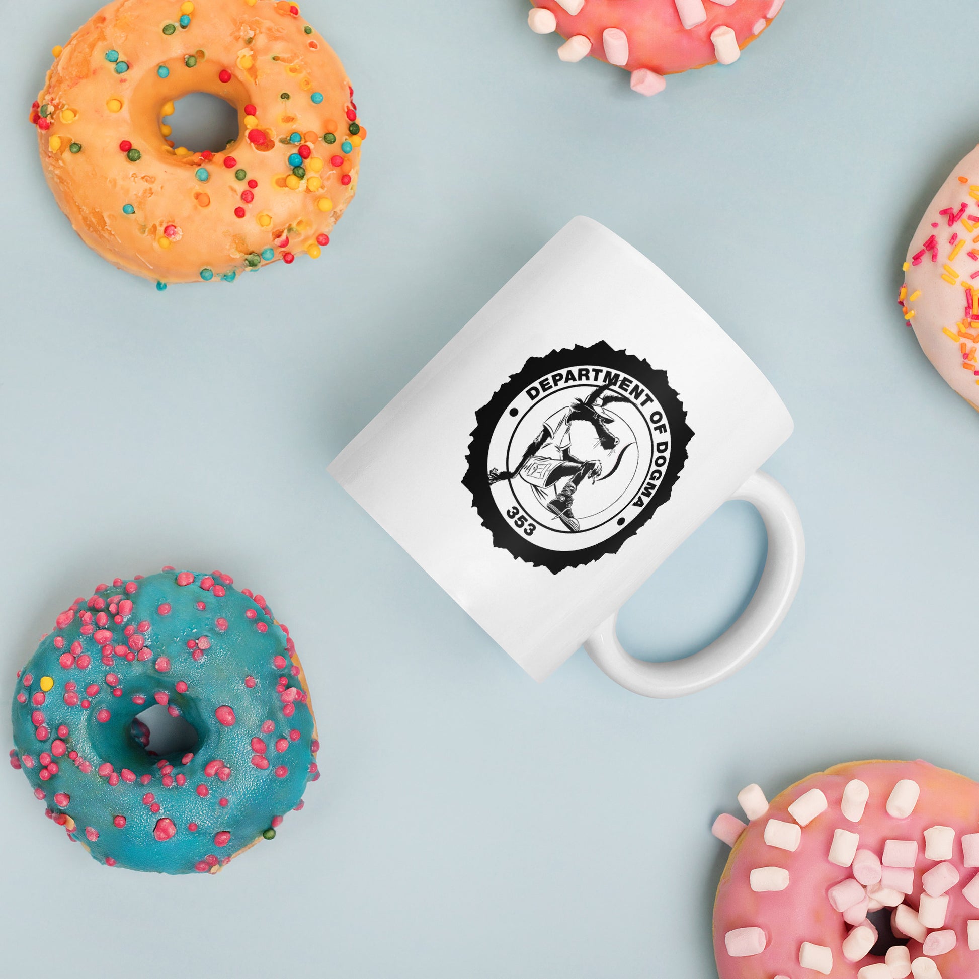 White mug with a black logo surrounded by colorful donuts on a light blue background