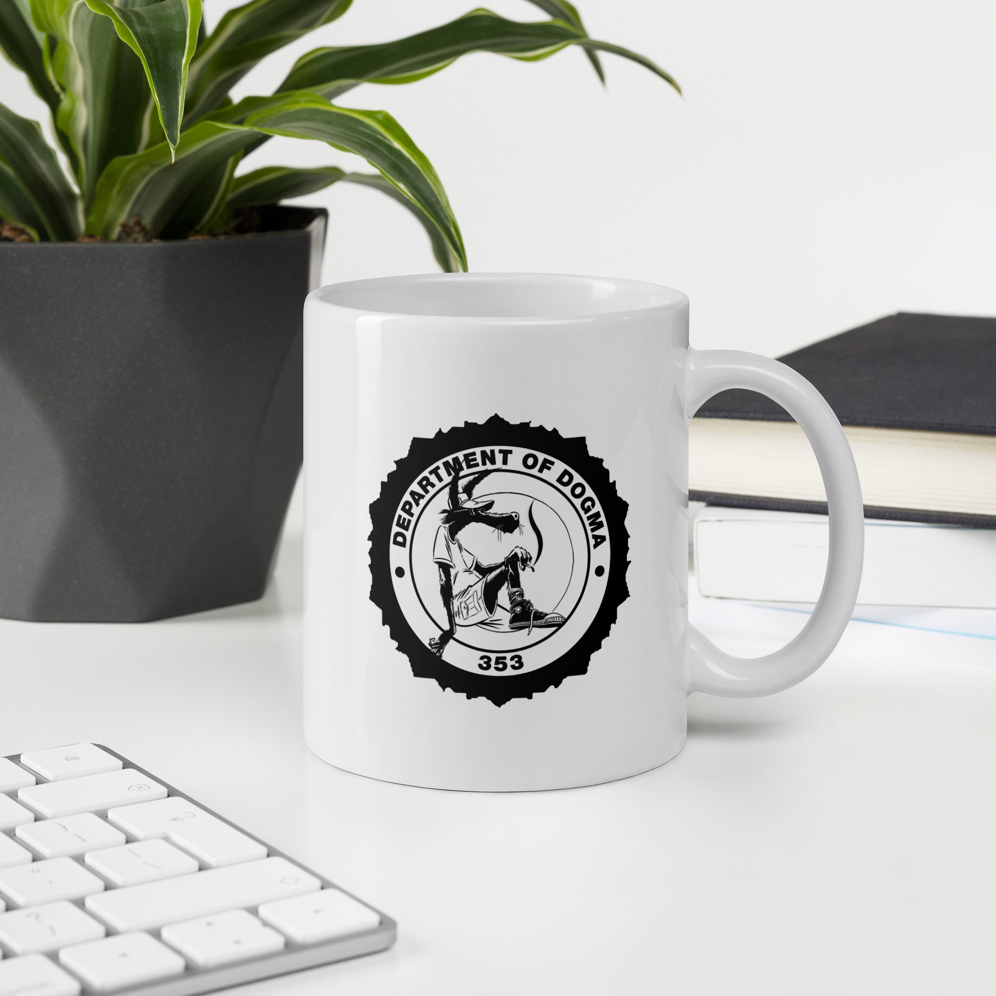 White mug with 'Department of Dogma' design on a desk with a plant and books in the background